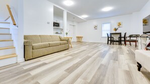 A spacious living area with a beige sofa, wooden flooring, a dining table with chairs, and a kitchen in the background. - Ludlow Townhome: 3 Mi to Okemo Mountain! (Ludlow)