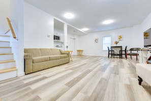 A spacious living area with a beige sofa, wooden flooring, and a kitchen in the background.