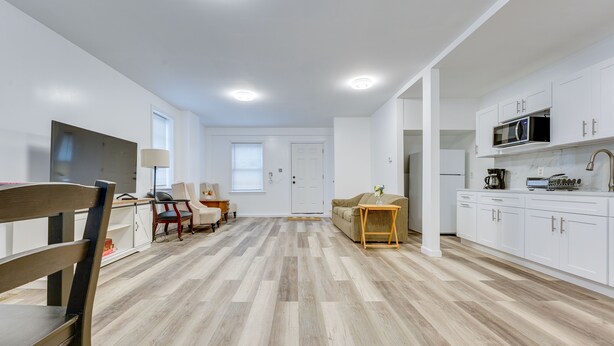 A modern kitchen with white cabinets, a microwave, and a coffee maker. There is a wooden dining table with chairs and a sofa in the living area. - Ludlow Townhome: 3 Mi to Okemo Mountain! (Ludlow)