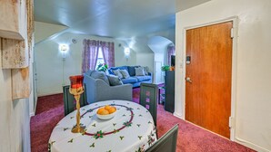 Una sala de estar acogedora con un sofá azul, una mesa de comedor con frutero, y una puerta de madera.