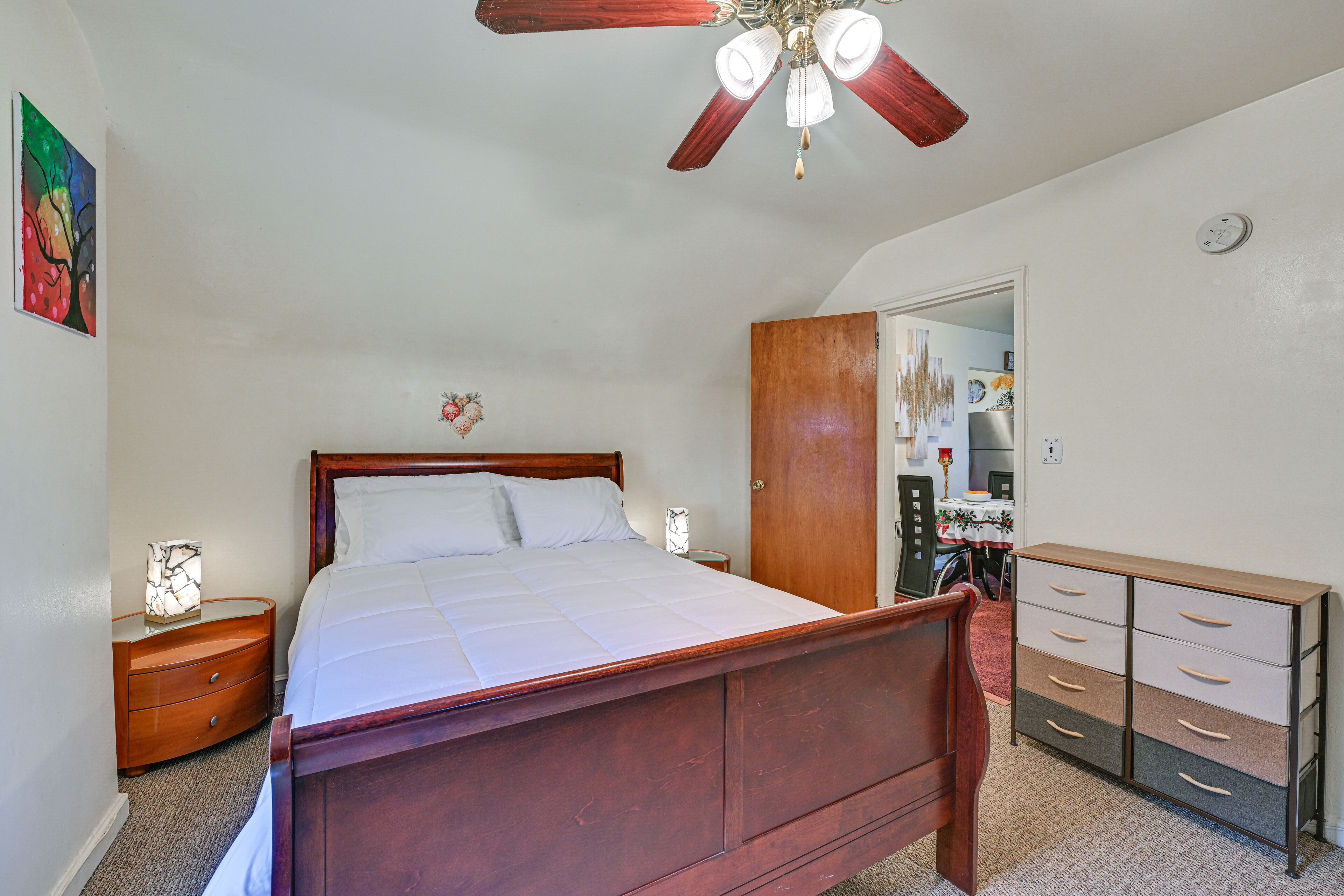 A bedroom with a wooden bed, a nightstand, a dresser, and a ceiling fan.