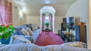 Sala de estar con sofá, televisor, planta en maceta y vista a través de un arco.