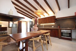 A kitchen with wooden cabinets, a dining table with chairs, a hanging light fixture, and built-in appliances.