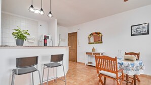 A kitchen with a white countertop, two bar stools, a dining table with a floral tablecloth, and a wooden chair.