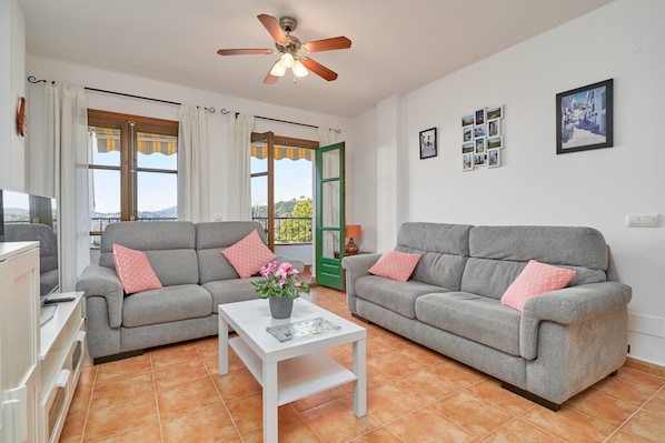 A living room with two grey sofas, a white coffee table, a ceiling fan, and a view through a window.