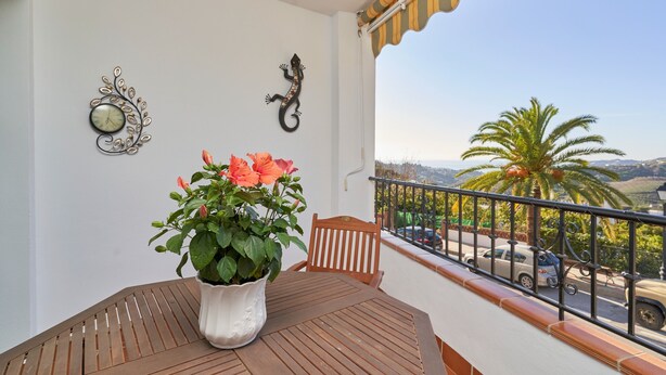 A balcony with a wooden table, a potted plant, a wall clock, and a decorative wall piece.