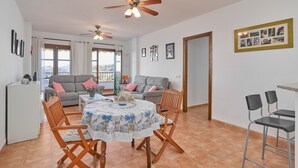 A living area with a sofa, a dining table with chairs, a ceiling fan, and a view through a window.