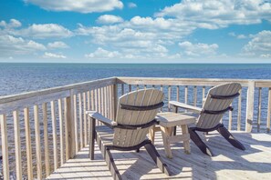 Une terrasse en bois avec deux chaises Adirondack donnant sur une étendue d’eau, sous un ciel dégagé.