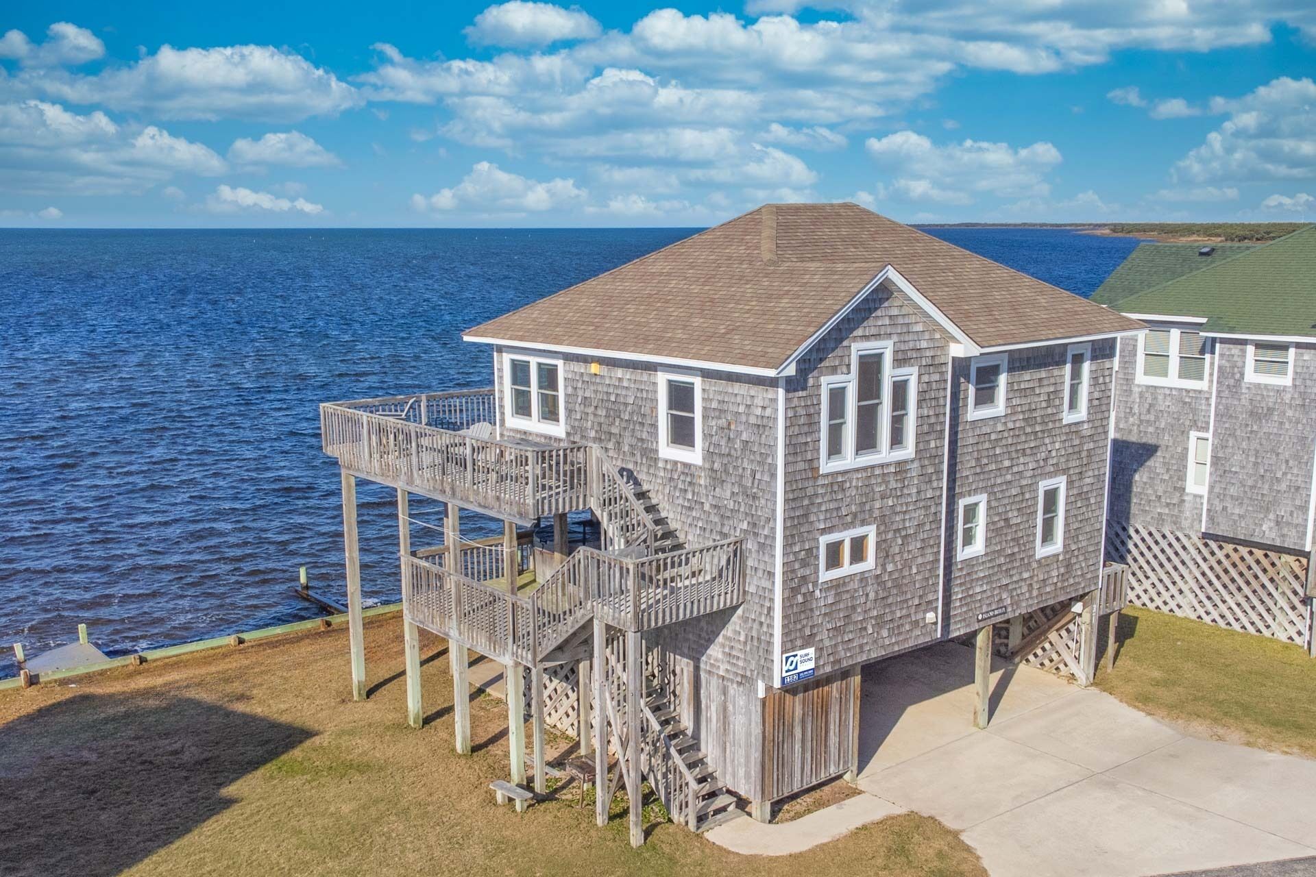 A two-story wooden house with a balcony, located near a body of water.