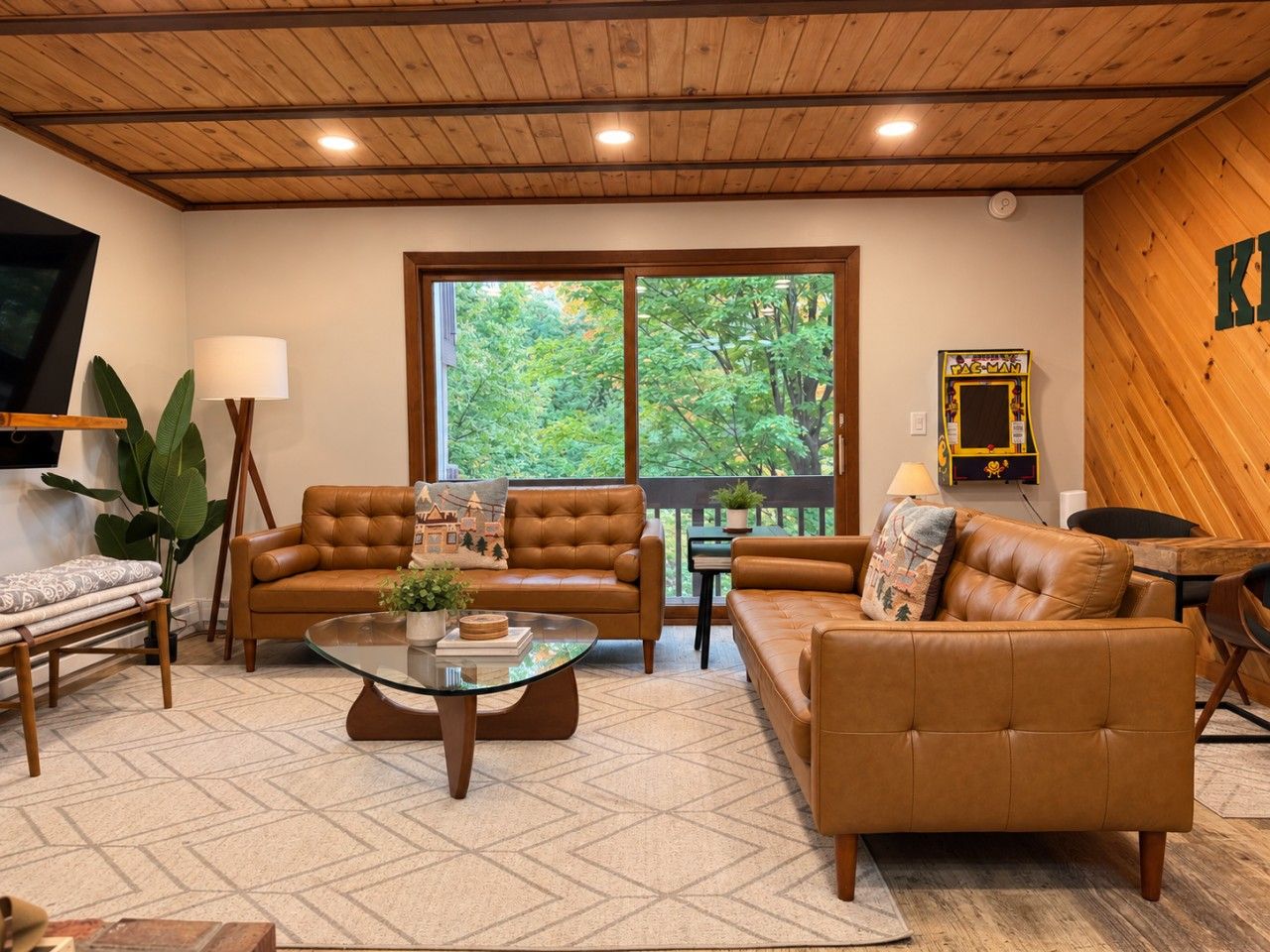 A cozy living room with leather sofas, a glass coffee table, and a large window offering a view of trees.