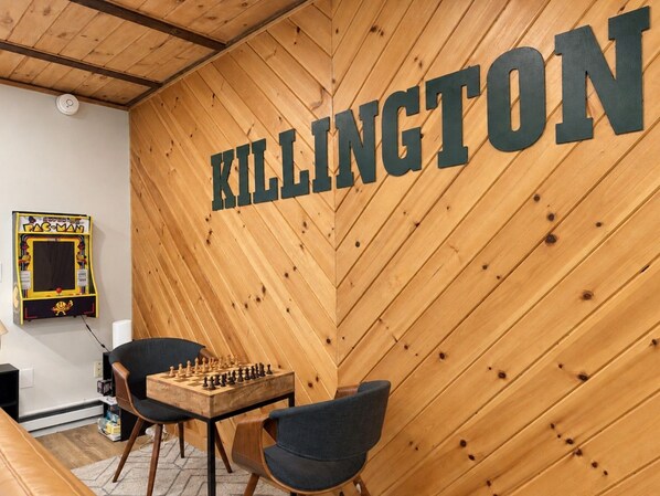 Una habitación con una pared de madera que muestra la palabra 'KILLINGTON' en letras grandes, una mesa de fútbol de mesa y una máquina arcade de Pac-Man.