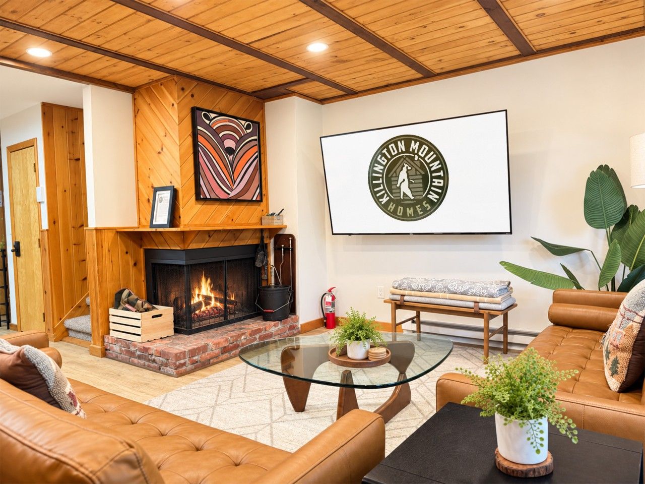 A cozy living room with a fireplace, leather sofas, a glass coffee table, and a large framed logo on the wall.