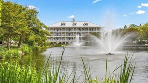 Et hotel med en stor bygning, en sø med springvand og frodig beplantning.