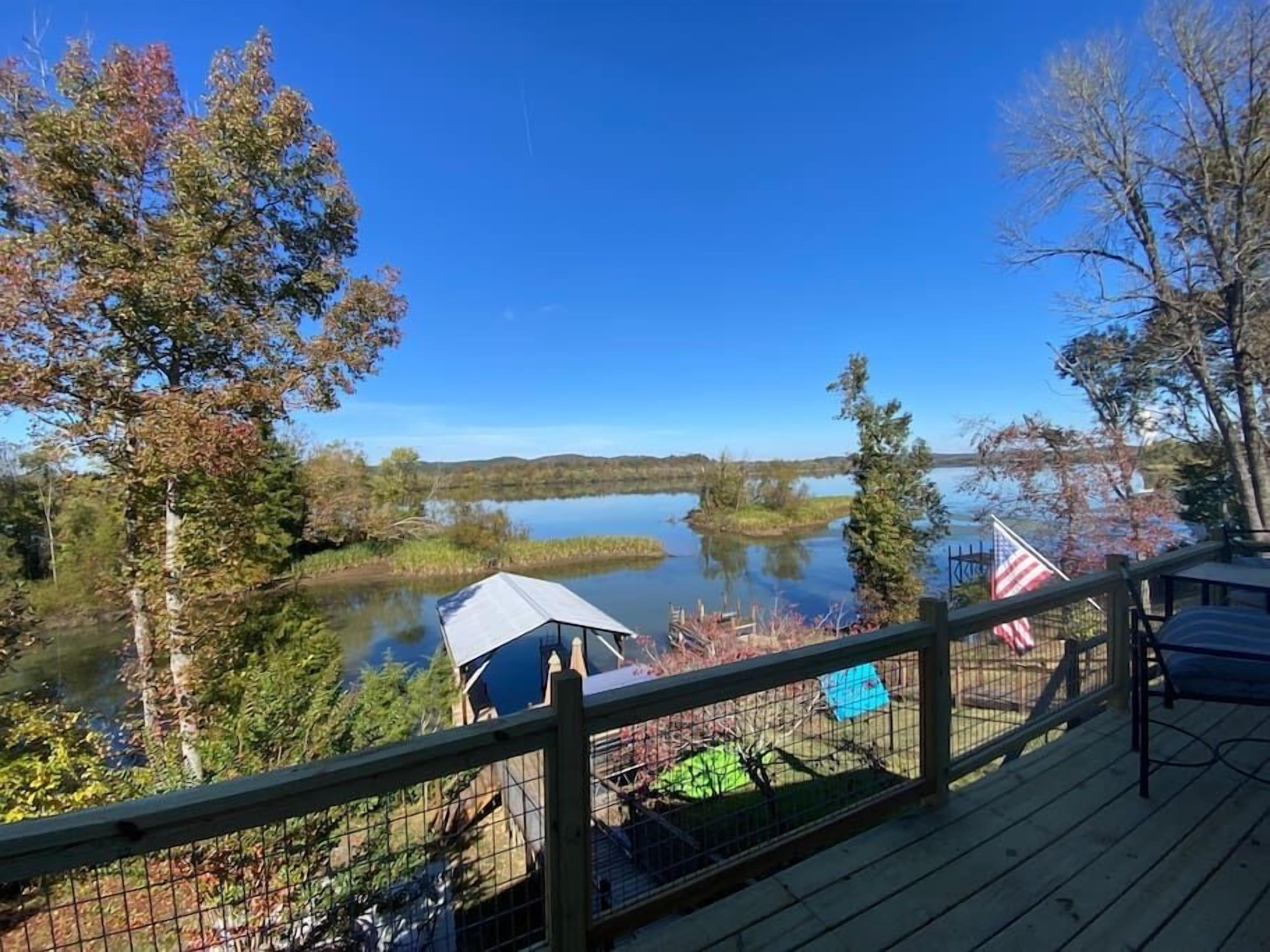 Una terraza con vista a un lago, rodeada de árboles y una pequeña bandera estadounidense.