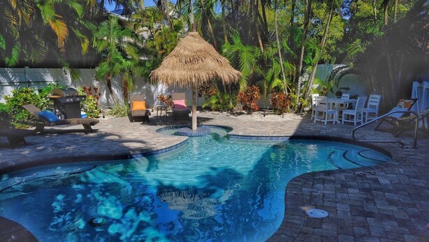 A swimming pool with a thatched roof structure, surrounded by lounge chairs and tropical plants.