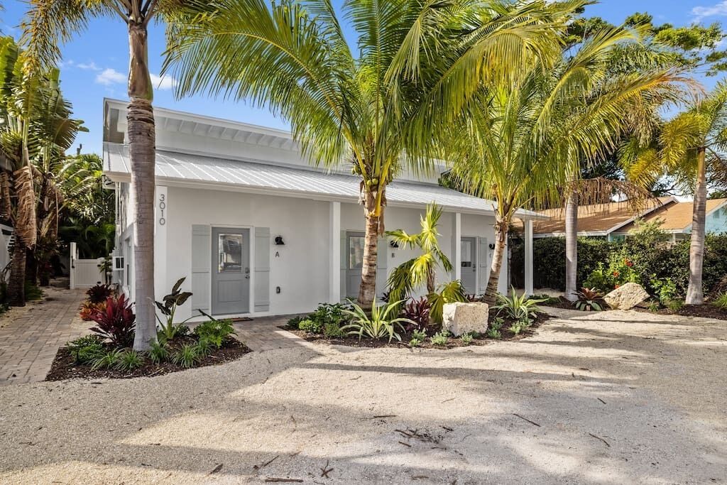 A white building with a number '3010' on the side, surrounded by palm trees and a landscaped garden.