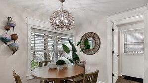Un comedor con una mesa redonda de madera, cuatro sillas, una lámpara colgante, un espejo grande y una planta en maceta.