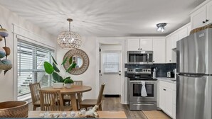 Una cocina moderna con armarios blancos, electrodomésticos de acero inoxidable y un comedor con mesa y sillas de madera.