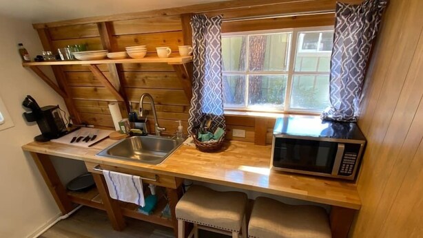 Une cuisine compacte dotée d’un plan de travail en bois, d’un évier, d’un four à micro-ondes et d’une fenêtre agrémentée de rideaux à motifs.