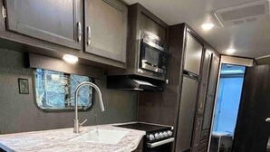 A compact kitchen with dark cabinetry, a built-in microwave, and a stove.