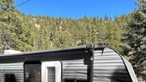 A motorhome parked outdoors with a ramp leading to the entrance, surrounded by trees.