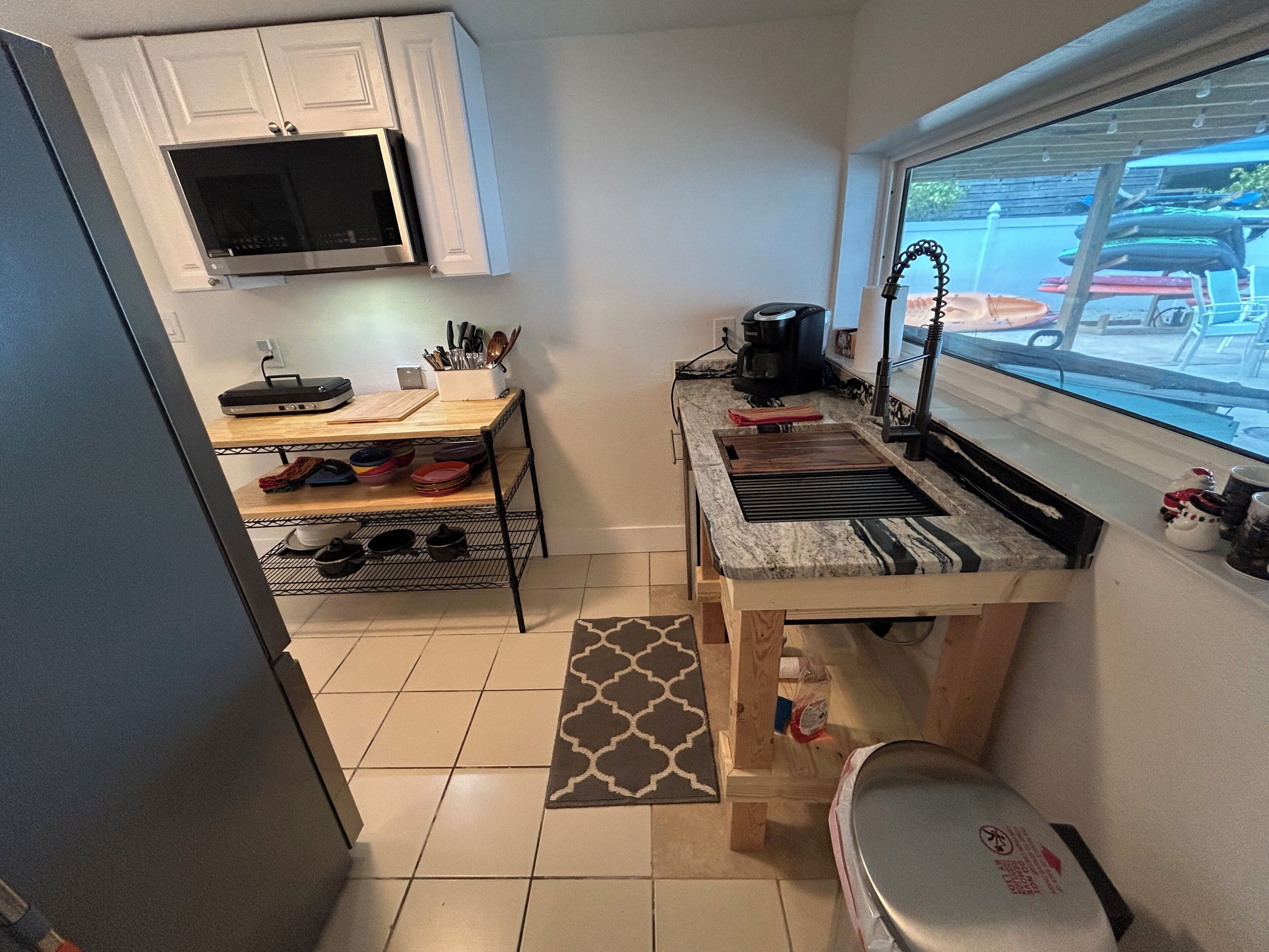 A compact kitchen with white cabinets, a microwave, a coffee maker, and a window with a view of parked cars outside.