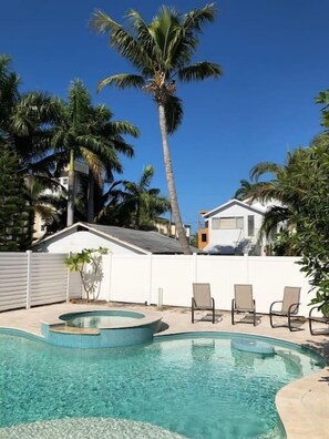 Ein Pool mit gewölbter Kante, umgeben von Palmen und einem weißen Zaun.