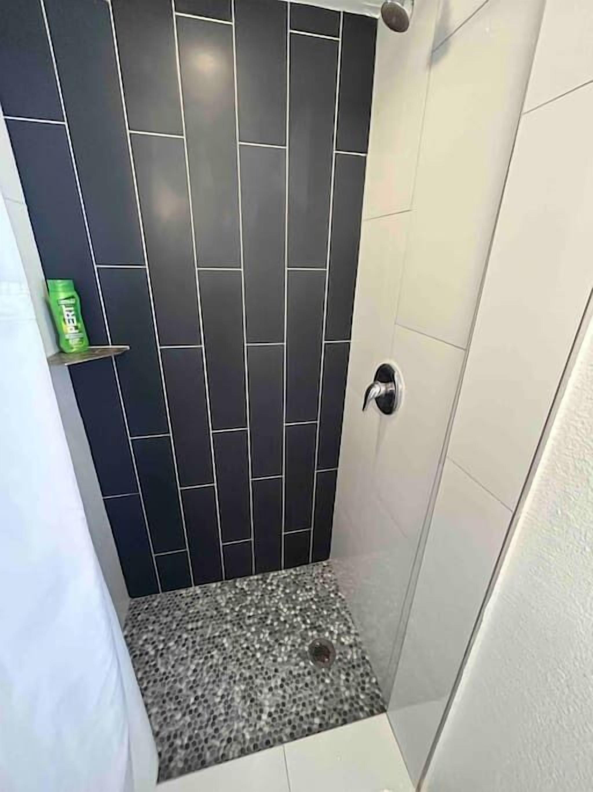 A small, modern bathroom with dark tiled walls, a granite floor, and a white door.