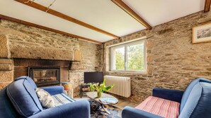 A stone-walled room with a fireplace, two blue armchairs, a small table with a plant, and a window with a view of trees. - Holiday Home 'Maison 6 Personnes Avec Piscine' with Private Pool and Wi-Fi (Le conquet)