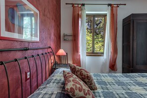 Quarto com cama, mesa de cabeceira, luminária, janela com cortinas e guarda-roupa.