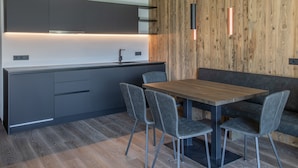 A modern kitchen with grey cabinets, a wooden accent wall, a wooden dining table with four chairs, and pendant lighting. - Apartment 'Köfele Lodge Sepp' with Mountain View, Shared Pool and Wi-Fi (Partschins)