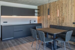 Una cocina moderna con gabinetes grises, una pared de acento de madera, una mesa de comedor de madera con cuatro sillas e iluminación colgante.