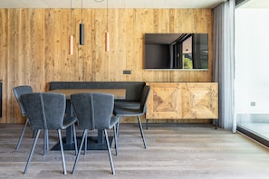 A modern dining area with a wooden wall, a large TV, and a view of the outdoors. - Apartment 'Köfele Lodge Sepp' with Mountain View, Shared Pool and Wi-Fi (Partschins)