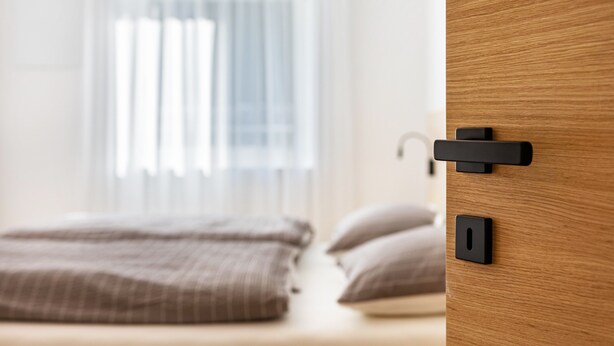 Une chambre à coucher avec un lit, une porte en bois et une fenêtre avec des stores.