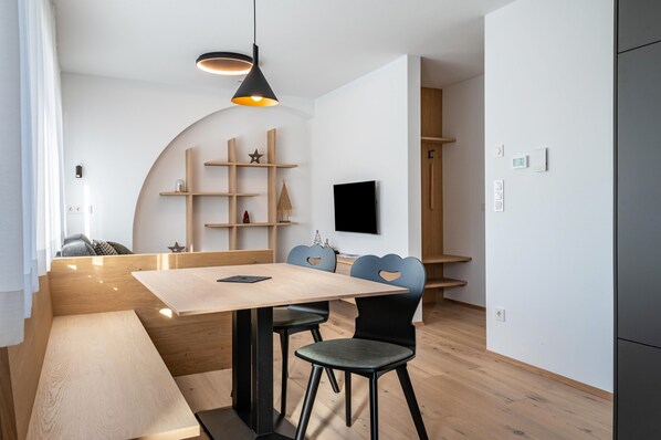 A modern dining area with a wooden table, black chairs, a hanging light fixture, and a TV mounted on the wall.