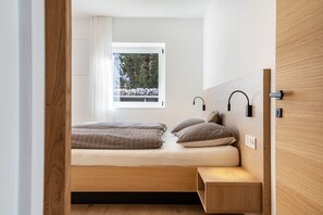 A bedroom with a bed, a window with curtains, a bedside table, and a wall-mounted light fixture.