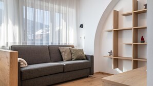 Un salon moderne avec un canapé gris, des étagères en bois et une fenêtre ornée de rideaux légers.
