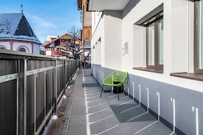 A narrow outdoor corridor with a metal fence, a green chair, and a building with a white facade and large windows.