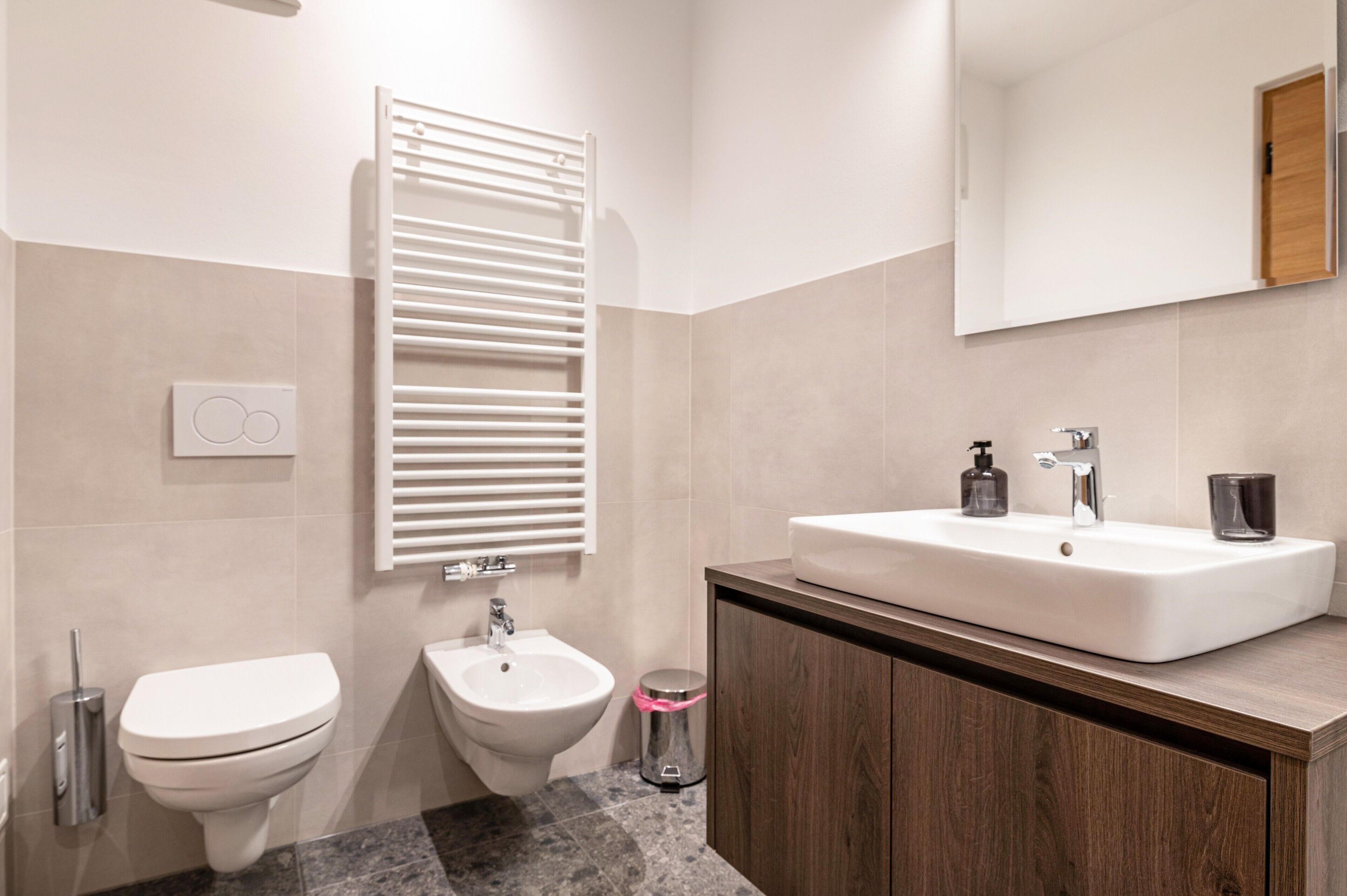 A modern bathroom with a toilet, bidet, vanity with a sink, and a mirror.