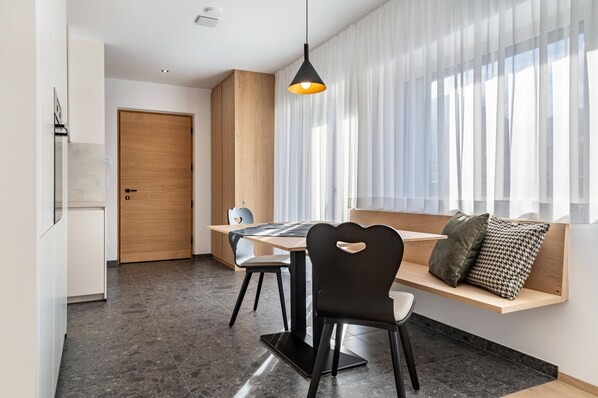 Un espace repas moderne avec une porte en bois, une table entourée de chaises, un luminaire suspendu et un banc agrémenté de coussins.