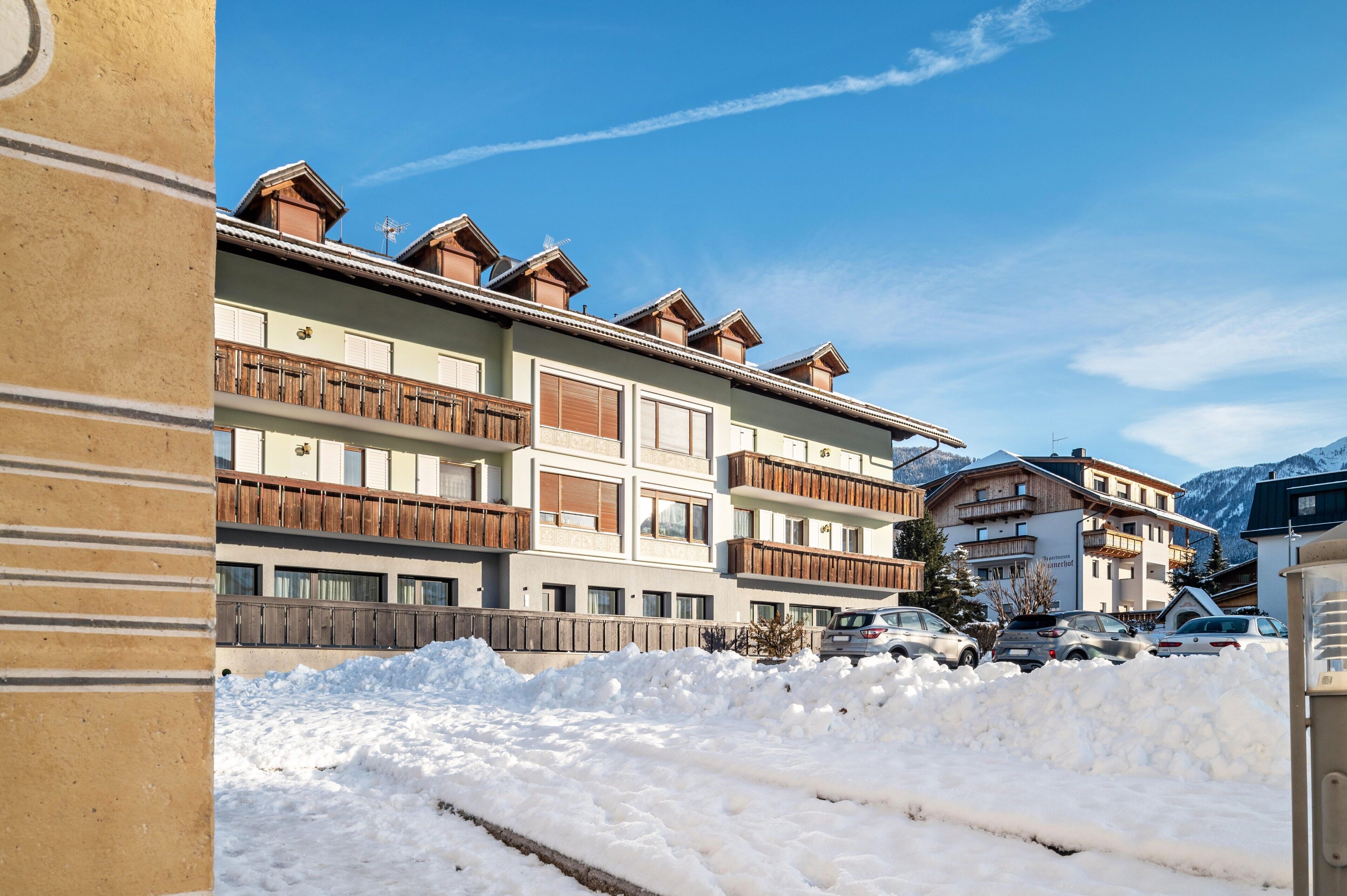 A multi-story hotel with balconies, a snow-covered ground, and mountains in the background.