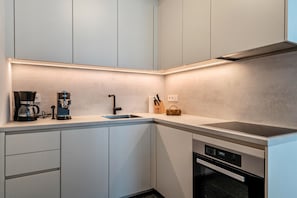 Et moderne køkken med indbygget ovn, kaffemaskine og et knivdisplay.