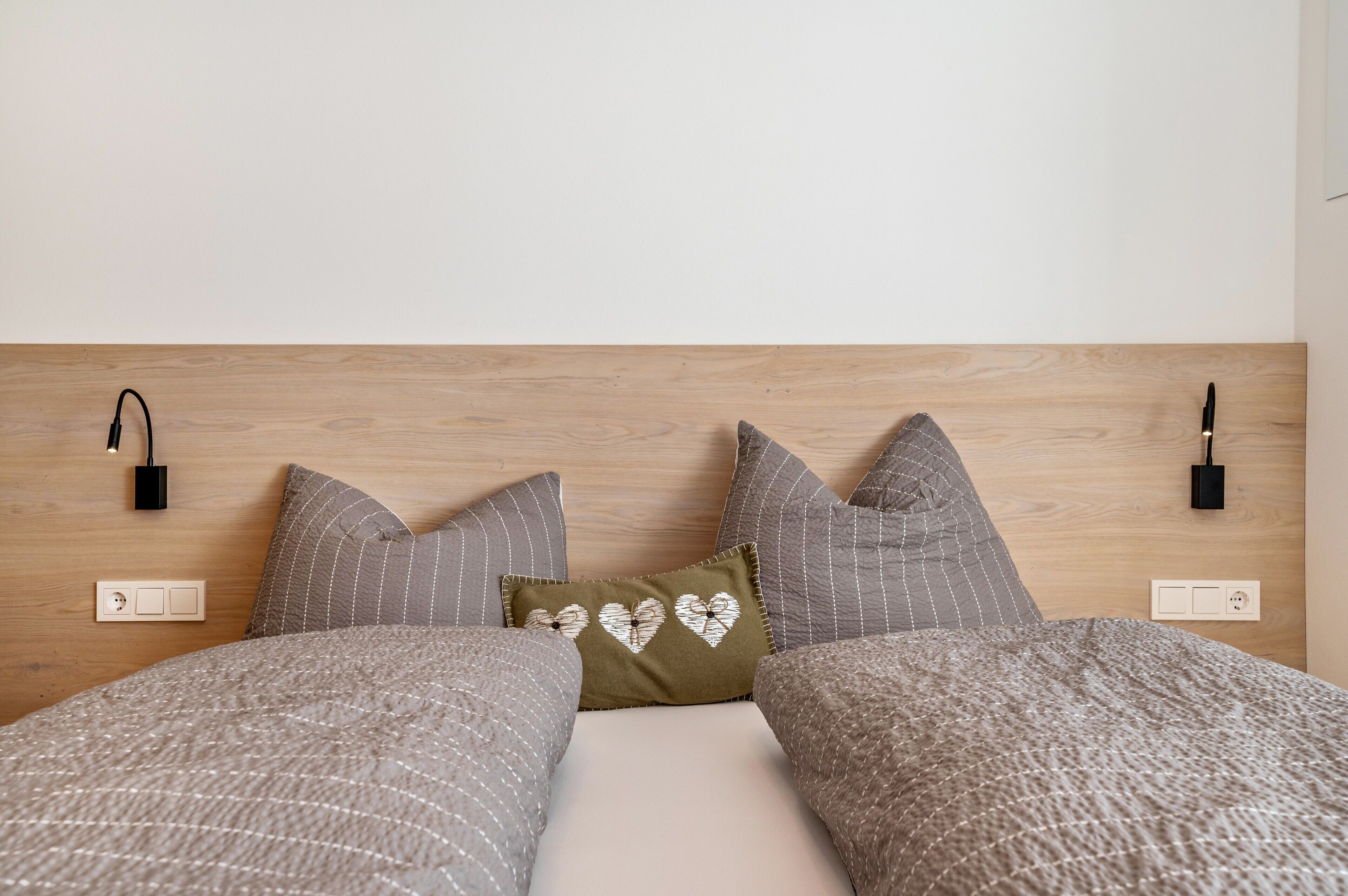 A bed with a wooden headboard, two bedside lamps, and a power outlet on the wall.