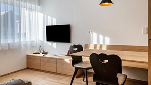 Un salon moderne avec un téléviseur à écran plat, une table à manger en bois, des chaises en forme de cœur, un petit meuble et une suspension.
