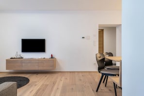 A modern living room with a flat-screen TV, wooden cabinet, and dining area with chairs.