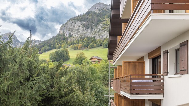 A multi-story building with wooden balconies, a mountain backdrop, and a view of a green valley. - Apartment 'Appartement Spacieux 6 Personnes' with Mountain View, Private Terrace and Wi-Fi (LE GRAND BORNAND)
