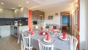 A modern kitchen with built-in appliances, a dining area with a table set for four, and a cozy living room with a sofa and a fireplace. - Apartment 'Appartement Spacieux 6 Personnes' with Mountain View, Private Terrace and Wi-Fi (LE GRAND BORNAND)