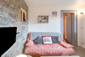 A cozy room with a stone wall, a checkered sofa, a fireplace, and a wooden door.