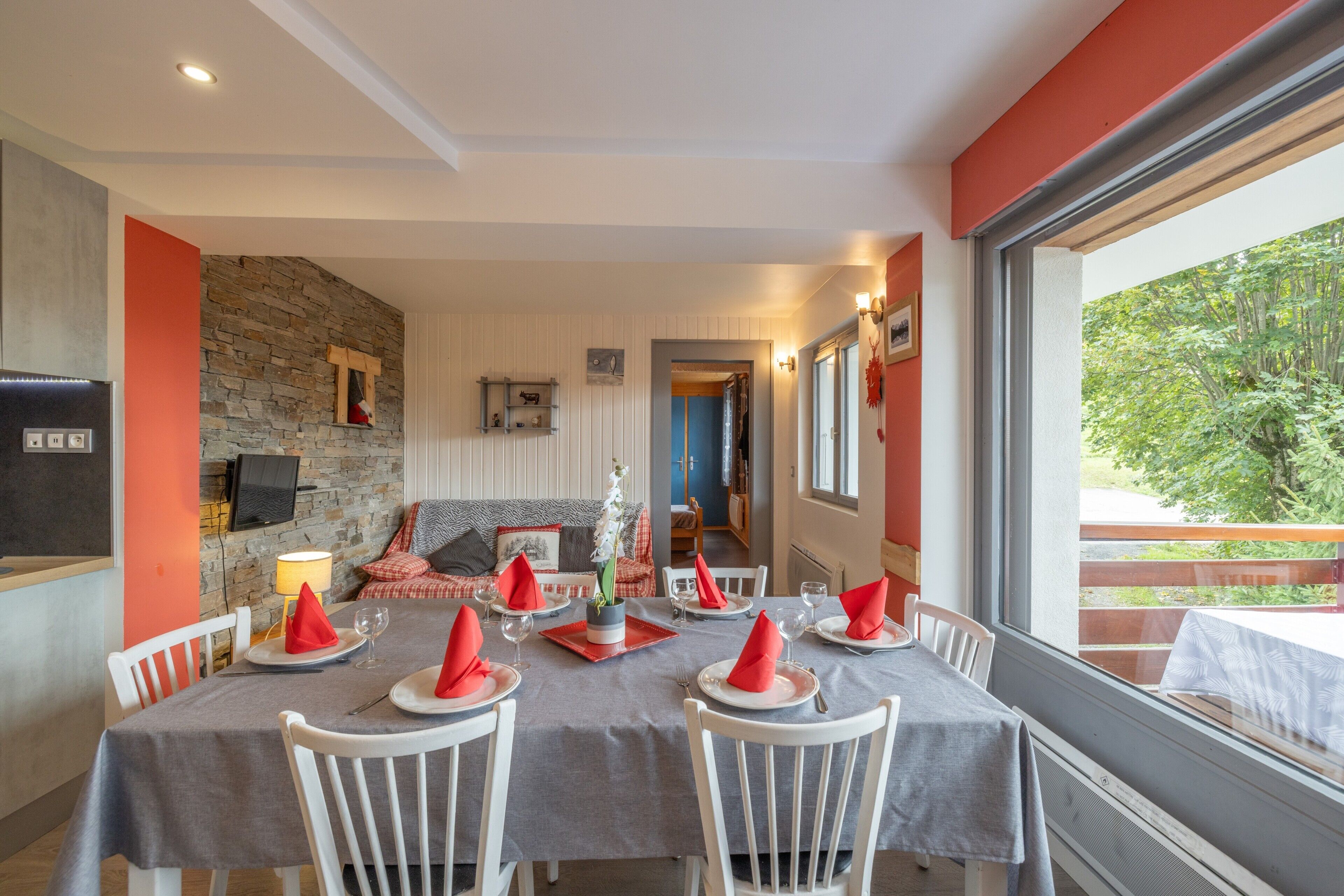 A dining area with a stone wall, a television, and a view of greenery outside.