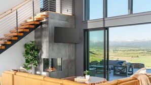 A modern living room with a sofa, a fireplace, and a large window overlooking a scenic landscape. - Basecamp Stays: Lux Retreat, Epic Views, & Hot Tub (Tetonia)